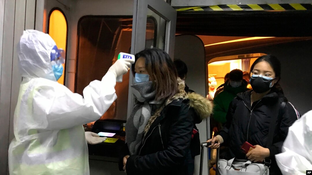 Health Officials in hazmat suits check body temperatures of passengers arriving from the city of Wuhan at the airport in Beijing, China, Jan. 22, 2020.