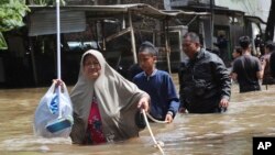 Warga berpegangan pada tali untuk melalui jalanan yang tergenang banjir di Tangerang, Banten, Kamis (2/1).