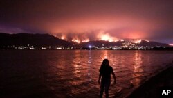 Seorang anak bermain di air sambil menyaksikan kebakaran lahan Cleveland National Forest di Lake Elsinore dari kejauhan, California, 8 Agustus 2018.