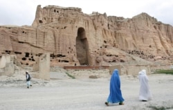 FILE - Two women walk past the cliffs that once held giant Buddhas destroyed by the Taliban in 2001 in Bamiyan, central Afghanistan, June 17, 2009.
