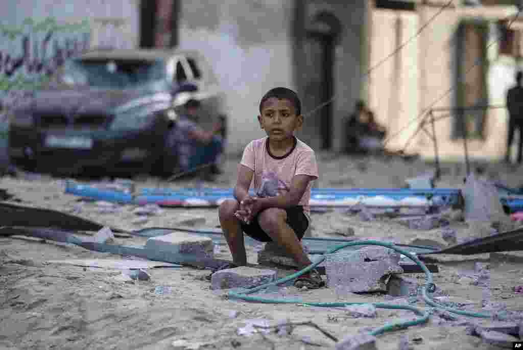 A Palestinian boy sits looking at others inspecting the damage of their shops following Israeli airstrikes on Jabaliya refugee camp, northern Gaza Strip.