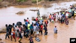 FILE - People wade over flood waters after a section of road was destroyed by floods at Mororo, border of Tana River and Garissa, North Eastern Kenya, November 30, 2023.