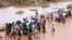 FILE - People wade over flood waters after a section of road was destroyed by floods at Mororo, border of Tana River and Garissa, North Eastern Kenya, November 30, 2023.
