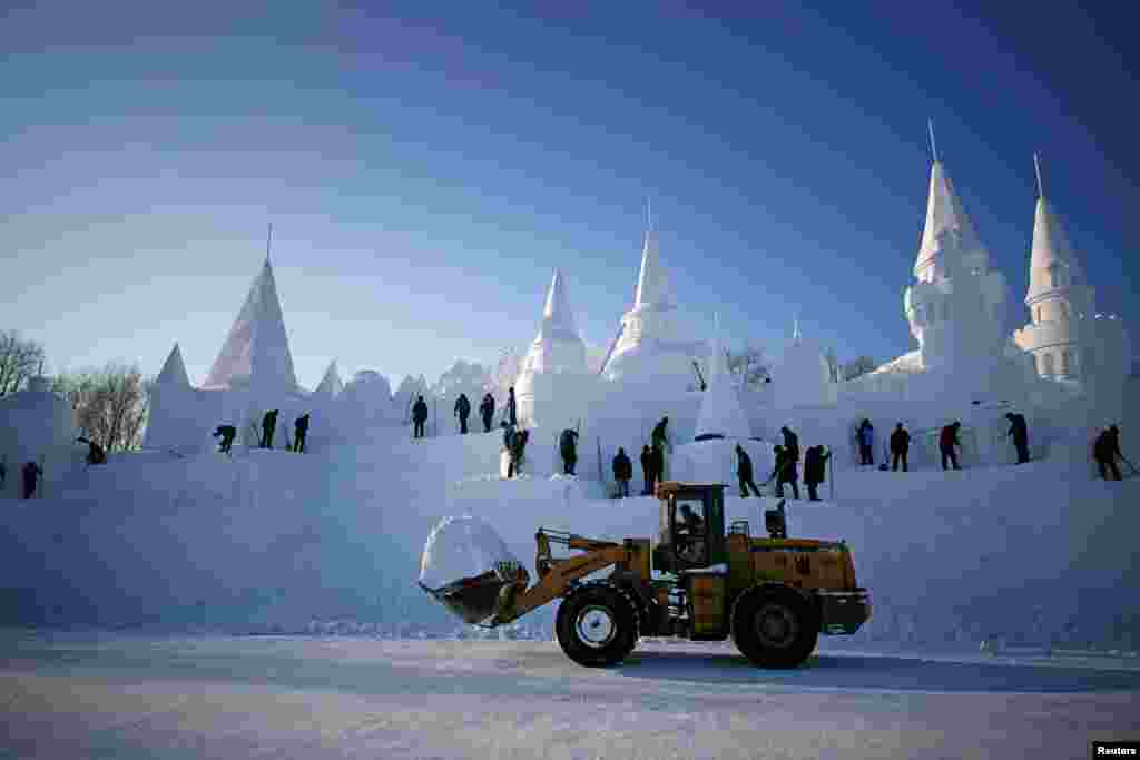زیرِ نظر تصویر میں مجسمے بنانے کے لیے درکار برف ٹریکٹر کے ذریعے لائی جا رہی ہے جب کہ پس منظر میں کئی کاریگر اپنے کام میں مصروف ہیں۔