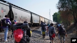 Migrantes caminan junto a un tren con dirección al norte, esperando poder subirse a él, en Huehuetoca, México, el viernes 12 de mayo de 2023. 