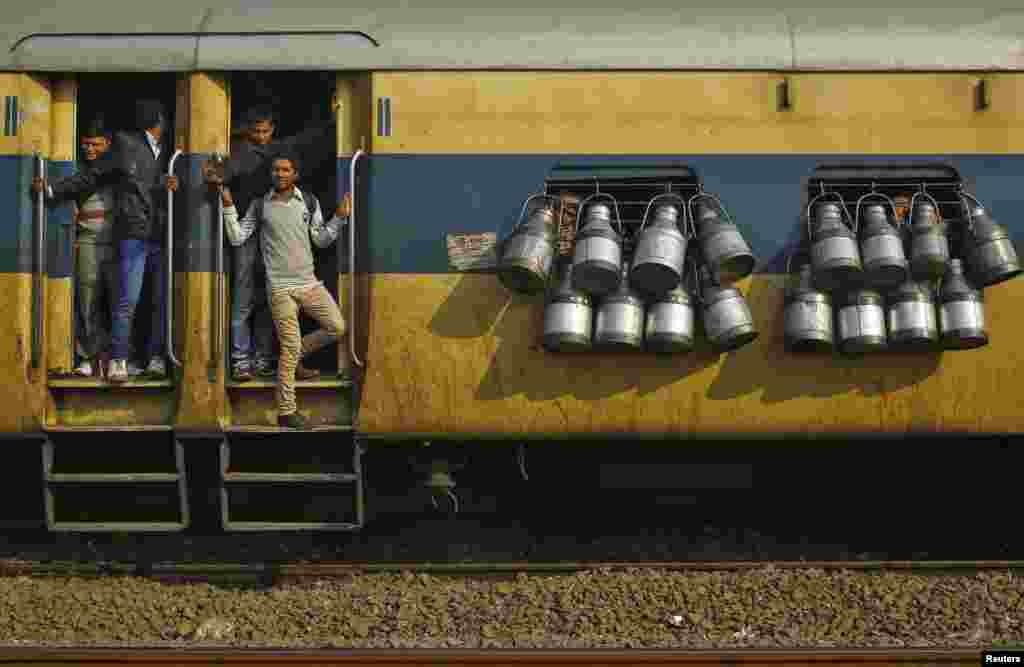 Commuters stand on the door of a passenger train as milk containers hang on the windows in Ghaziabad, on the outskirts of New Delhi, India.