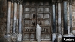 Seorang pria berdiri di depan pintu Gereja Makam Suci (Church of the Holy Sepulcher) yang tertutup pada Jumat Agung di tengah wabah penyakit coronavirus (COVID-19), di Kota Tua Yerusalem, 10 April 2020. REUTERS / Ammar Awad