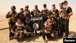 Kurdish Peshmerga fighters pose with an Islamic State flag, which they pulled down after capturing Mount Batnaya, near Zummar, Sept. 20, 2014.