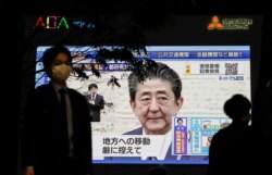 A pedestrian wearing a protective mask walks past a large screen on a building showing Japan's Prime Minister Shinzo Abe declaring a state of emergency, following the coronavirus disease (COVID-19) outbreak, in Tokyo, Japan, April 7, 2020.