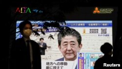 A pedestrian wearing a protective mask walks past a large screen on a building showing Japan's Prime Minister Shinzo Abe declaring a state of emergency, following the coronavirus disease (COVID-19) outbreak, in Tokyo, Japan April 7, 2020.