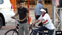 FILE - A Kurdish man and a woman wearing a T-shirt with the Kurdish flag printed on it ride their bikes in the northern city of Sulaimaniyah in the autonomous Kurdish region, July 21, 2009. 