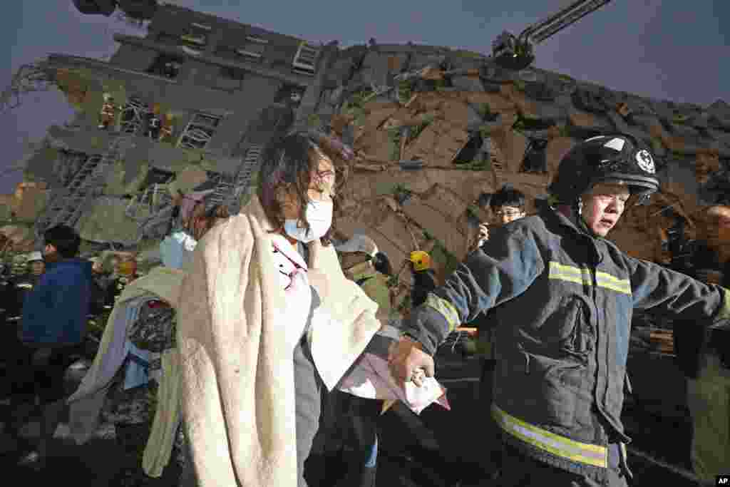 A woman is led by a rescue worker from the site of a damaged building.