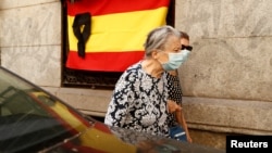 Women wearing protective face masks walk past a Spanish flag with a black ribbon for the victims of the coronavirus pandemic, in Madrid, Spain, May 22, 2020.