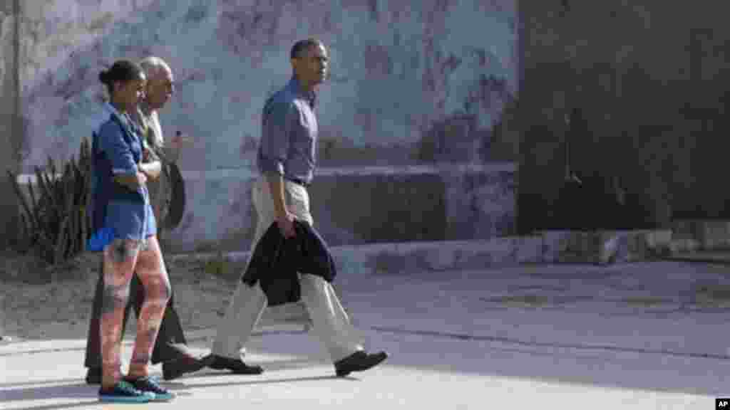 President Obama, his daughter Sasha Obama, and Ahmed Kathrada a former prisoner with Mandela, walk through the courtyard of the prison on Robben Island.