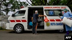 Seorang pasien virus corona (kiri) berbincang dengan petugas medis sebelum naik ke ambulans untuk pulang ke rumahnya dari RSUD Zainoel Abidin di Banda Aceh, 13 April 2020. (Foto: AFP)