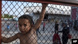 FILE - A child stands behind a fence at the Oreokastro camp, near the northern town of Thessaloniki, Greece, June 25, 2016.