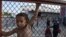 FILE - A child stands behind a fence at the Oreokastro camp, near the northern town of Thessaloniki, Greece, June 25, 2016.