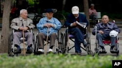 In this 2013 file photo, a group of elderly men take a rest on their wheelchairs at a park in Beijing. China passed law requiring people to visit or keep in touch with their elderly parents. (AP Photo/Andy Wong)
