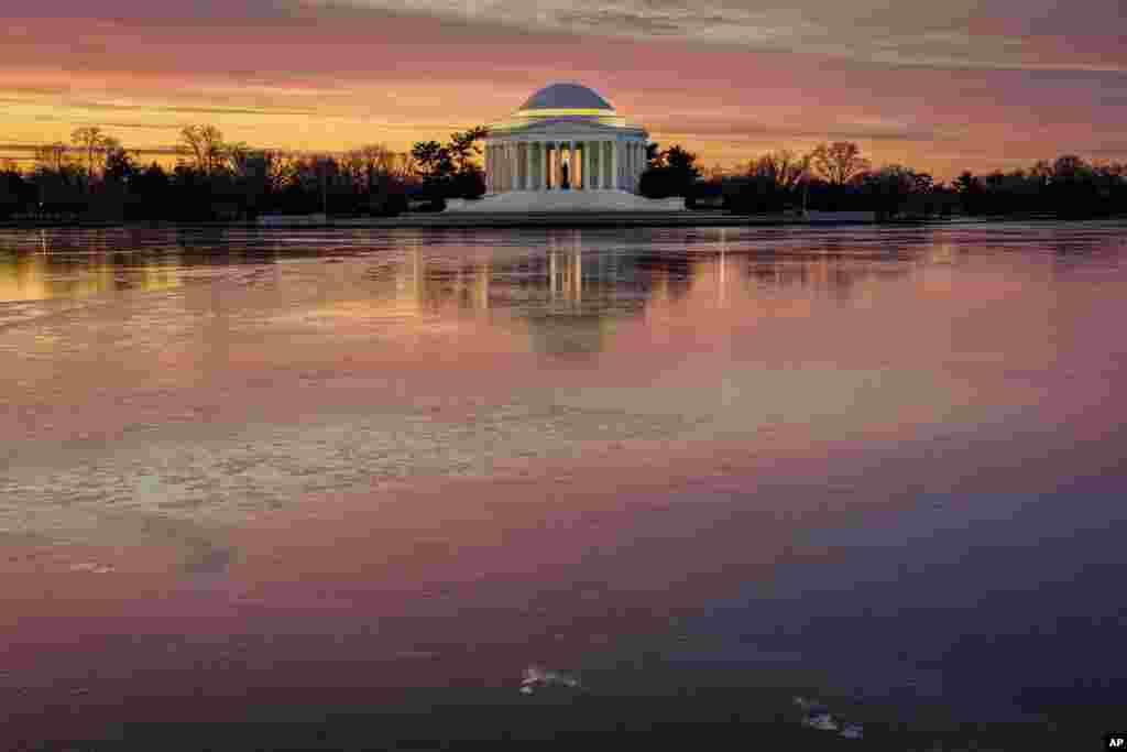 Refleksi sinar matahari terbit tampak pada permukaan air beku Danau Tidal Basin di depan Jefferson Memorial pada pagi hari yang dingin di kota Washington DC, Minggu (23/1). (Foto: AP)