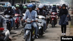 Seorang perempuan berjalan di trotoar, dilewati puluhan sepeda motor di Jakarta Selatan.