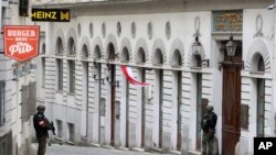 Un hombre lleva una corona de flores mientras pasa junto a los agentes de policía en Viena, Austria, el martes 3 de noviembre de 2020.