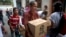 Una mujer en el vecindario de San Agustín, en Caracas, carga una caja de alimentos básicos como arroz, fréjoles, atún y leche en polvo, que entrega el gobierno de Venezuela bajo el programa CLAP (Comités Locales de Abastecimiento y Producción). Mayo 16 de 2018. Algunos votantes temen perder las entregas de alimentos subsidiados y empleos en el gobierno si no votan por el presidente Nicolás Maduro el próximo 20 de mayo.