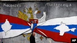 FILE - A man walks by graffiti that shows Serbian, left, and Russian flags with maps of Kosovo and Crimea in northern, Serb-dominated part of ethnically divided town of Mitrovica, Kosovo, Dec. 15, 2018. 
