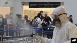 FILE - Passengers line up as workers wearing protective gear spray disinfectant as a precaution against the coronavirus outbreak, in the departure terminal at the Rafik Hariri International Airport, in Beirut, Lebanon, March 5, 2020.