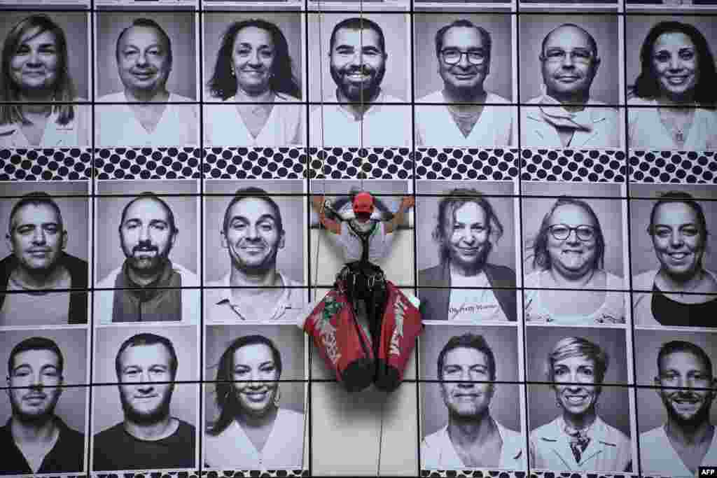 A worker pastes portraits of health care workers created on the facade of the Opera Bastille, at the initiative of the collective #ProtegeTonSoignant to pay tribute to caregivers during the COVID-19 epidemic, in Paris.