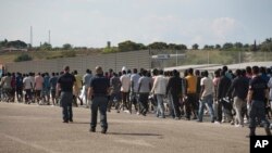 FILE - Italian border police escort sub-Saharan men on their way to a relocation center, after arriving in the Golfo Azzurro rescue vessel at the port of Augusta, in Sicily, Italy, June 23, 2017. 