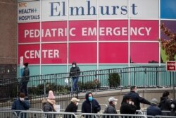 FILE - In this March 25, 2020, file photo, a woman exits a new coronavirus testing site while others wait in line at Elmhurst Hospital Center, in the Queens borough of New York.