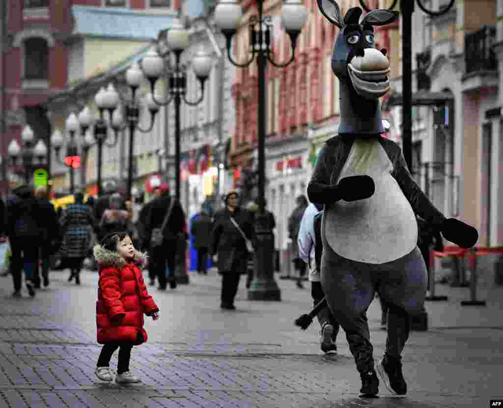 A young girl looks at a costumed character in downtown Moscow, Russia, Nov. 5, 2019.