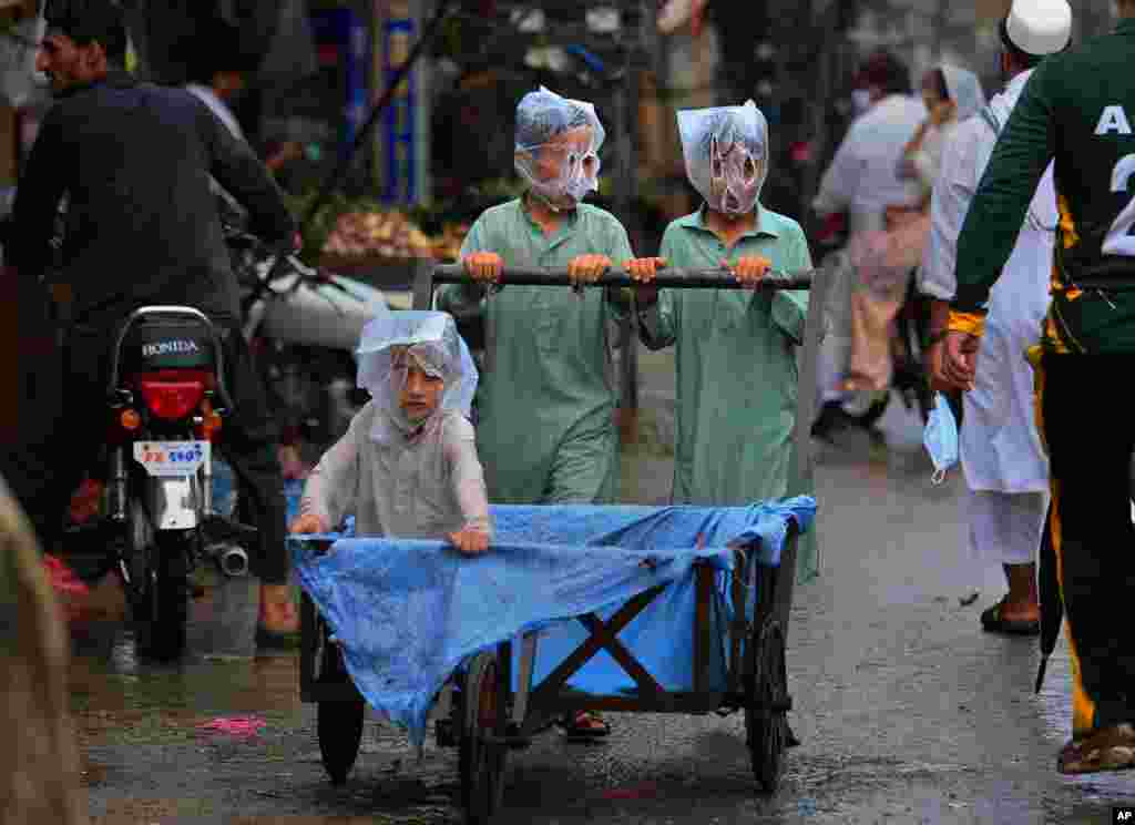 Boys cover their faces with plastic bags while pushing a handcart during rainfall in Peshawar, Pakistan.