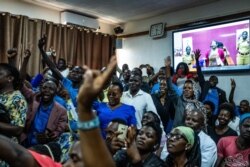 Supporters of jailed activist Stella Nyanzi gesture during her court proceedings near a screen showing her via video link, after she was charged guilty of cyber harassment against Uganda’s president, in a Kampala courtroom, Aug. 2, 2019.