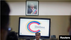 El embajador de Venezuela en Cuba, Alí Rodríguez Araque, hablando durante una conferencia de prensa bajo una fotografía del fallecido presidente de Venezuela Hugo Chávez.