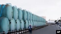Employees of Tokyo Electric Power Co. look at old tanks which used to store radioactive water at the Fukushima Daiichi nuclear power plant in Okuma town, Fukushima prefecture, northeastern Japan, Saturday, Feb. 27, 2021. (AP Photo/Hiro Komae)