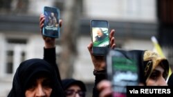 Iranian demonstrators hold up phones with pictures of the late Qassem Soleimani and Iraqi militia commander Abu Mahdi al-Muhandis, who were killed in an airstrike at Baghdad airport, in front of the U.N. office in Tehran, Iran, Jan. 3, 2020.