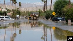 FILE - Firefighters use a skip loader to rescue a person from an assisted living center after the street was flooded with mud Monday, Aug. 21, 2023, in Cathedral City, Calif.