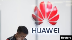 FILE - A staff member stands in front of a Huawei shop in Beijing, China, March 7, 2019. 