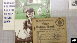 A World War II British ration card (R) rests on a flyer (C) that shows a woman operating machinery juxtaposed with a depiction of a family doing yard work, in a display at The International World War II Museum, in Natick, Mass., May 21, 2018. 
