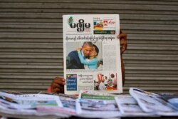 FILE - A woman holds up a Mizzima newspaper at a newspaper wholesale market in Yangon, Nov. 15, 2014.