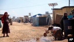 FILE - A refugee is seen scooping water from a puddle at a camp on the Syrian side of the border with Turkey, near the town of Atma, in Idlib province, Syria, April 19, 2020.
