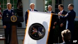 FILE- Gen. John "Jay" Raymond, President Trump, Vice President Pence, and Sec. of Defense Mark Esper, unfurl the U.S. Space Command flag during a ceremony to establishment of the U.S. Space Command in the Rose Garden of the White House, Aug. 29, 2019.