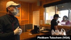 Staffers wear surgical masks and gloves as they prepare food for a customer through the to-go window at Thai House Restaurant in Gaithersburg, MD., March 29, 2020. 