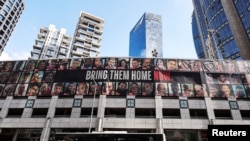 Un autobús con la leyenda en hebreo "Juntos venceremos" pasa junto a un cartel gigante que exige la liberación de los rehenes que fueron secuestrados durante el mortal ataque del 7 de octubre de 2023 contra Israel, en Ramat Gan, Israel, el 20 de noviembre de 2024.