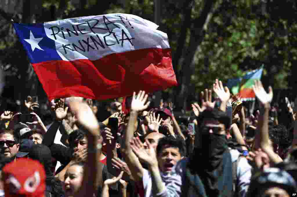 Los manifestantes ondean una bandera chilena, marcada con un mensaje que dice en español: &quot;Piñera renuncia&quot; durante una manifestación en Santiago, Chile, el lunes 21 de octubre de 2019.(Foto AP / Miguel Arenas).