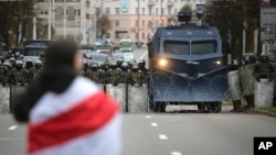 A protester draped in an old Belarusian national flag stands in front of a police line during an opposition rally to protest the official presidential election results in Minsk, Belarus, Sunday, Oct. 25, 2020. 