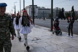 FILE - Tourists wearing protective masks watch the Presidential Guards in front of the parliament, in Athens, March 15, 2020.