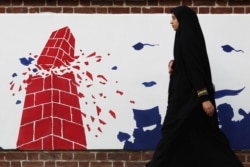 FILE - A woman walks past an anti-U.S. mural on the former U.S. Embassy's wall in Tehran, Iran, Jan. 7, 2020.