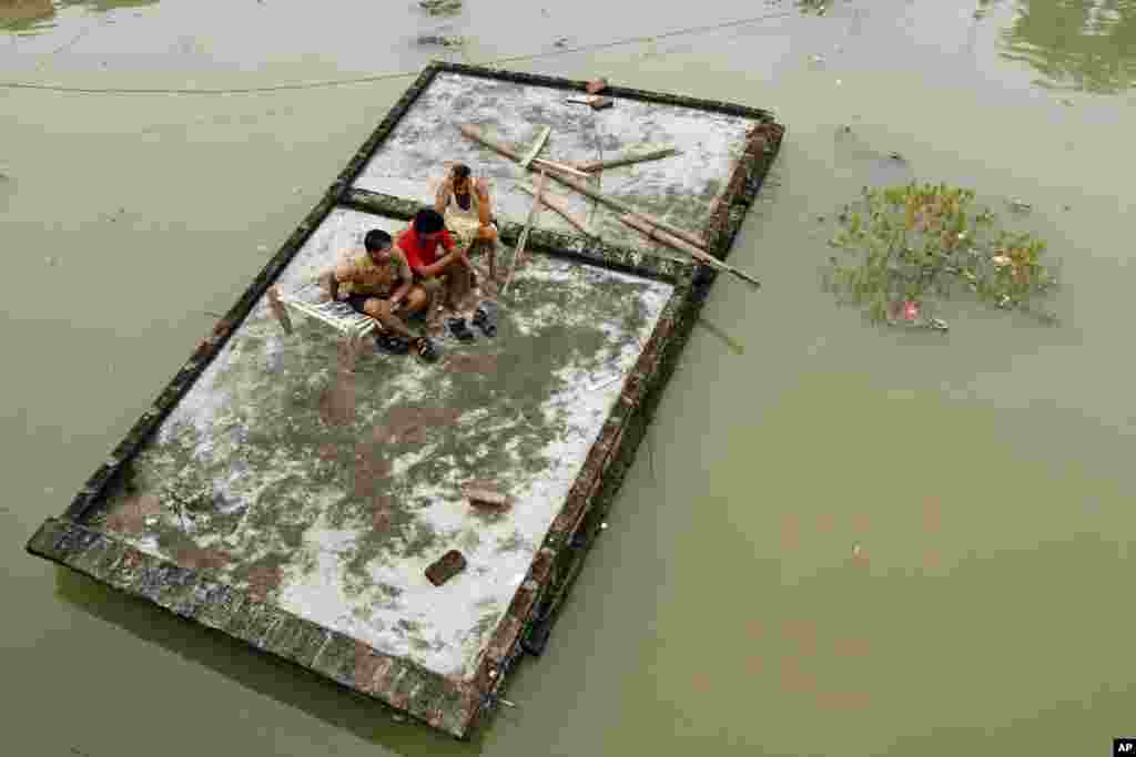 Tiga pria India duduk di atap rumah yang terendam banjir di Sungai Gangga setelah hujan lebat di Salori, India.